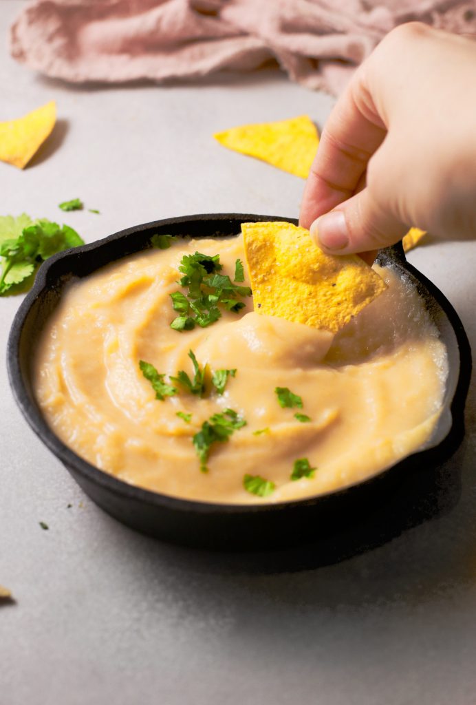 hand dipping a chip in vegan queso
