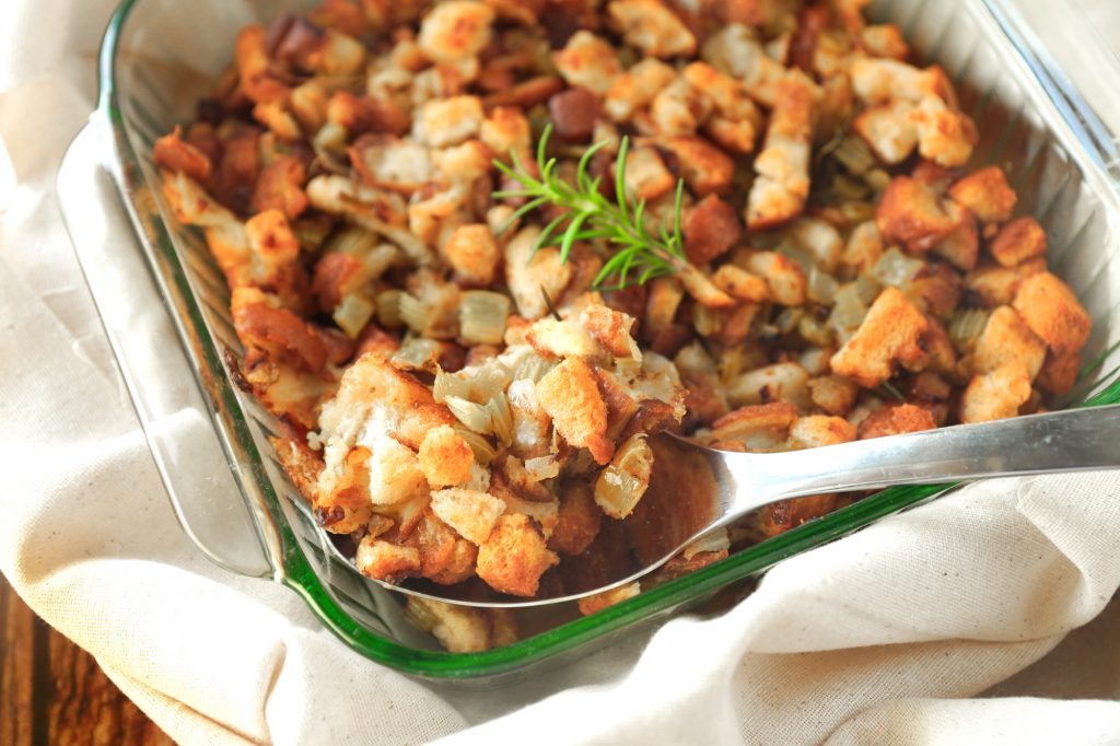 vegan bread stuffing being scooped out with serving spoon with plate sitting on a white towel