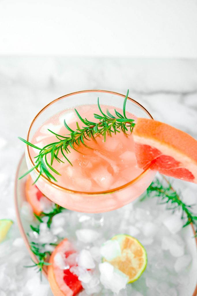 side view of grapefruit cocktail garnished with rosemary and lime