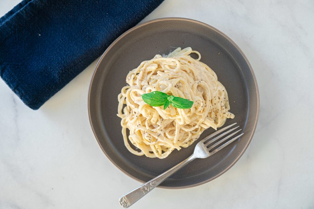 Straight down view of a fork on a plate full of vegan Alfredo pasta with basil.