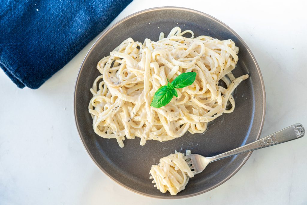 Straight view down of vegan alfredo sauce on pasta with fork on plate twirling pasta.