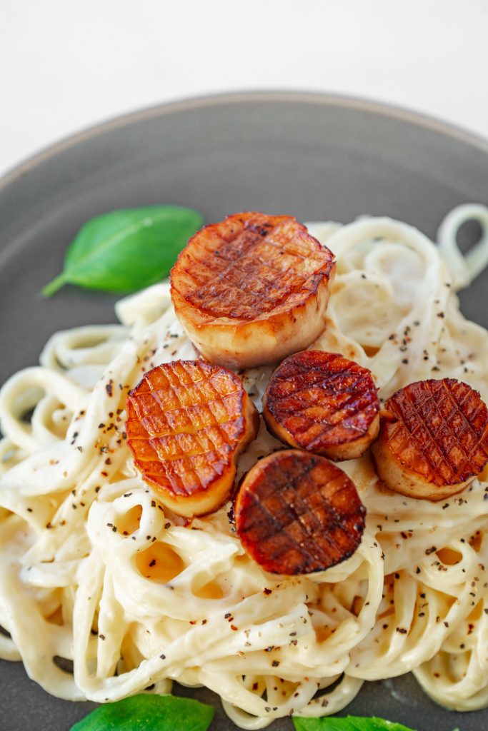 Grilled vegan scallops topping non-dairy alfredo sauce on pasta.
