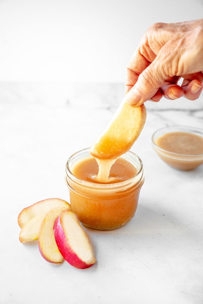 hand dunking apple spice into vegan caramel sauce