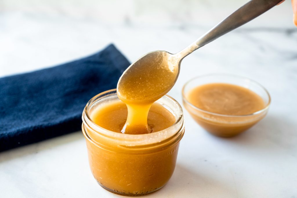 spoon holding vegan caramel sauce with some in the background