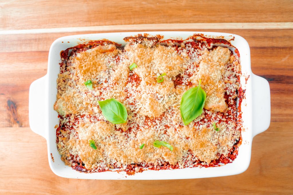 full dish of vegan eggplant parmesan with basil leaves