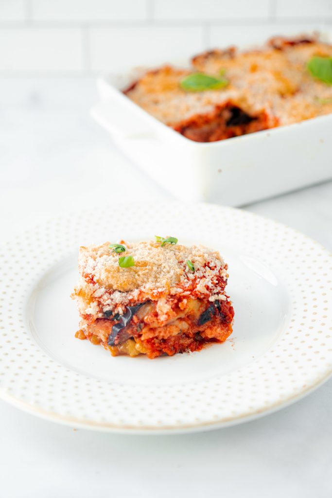 vertical image of a slice of vegan eggplant parmesan with casserole in the background