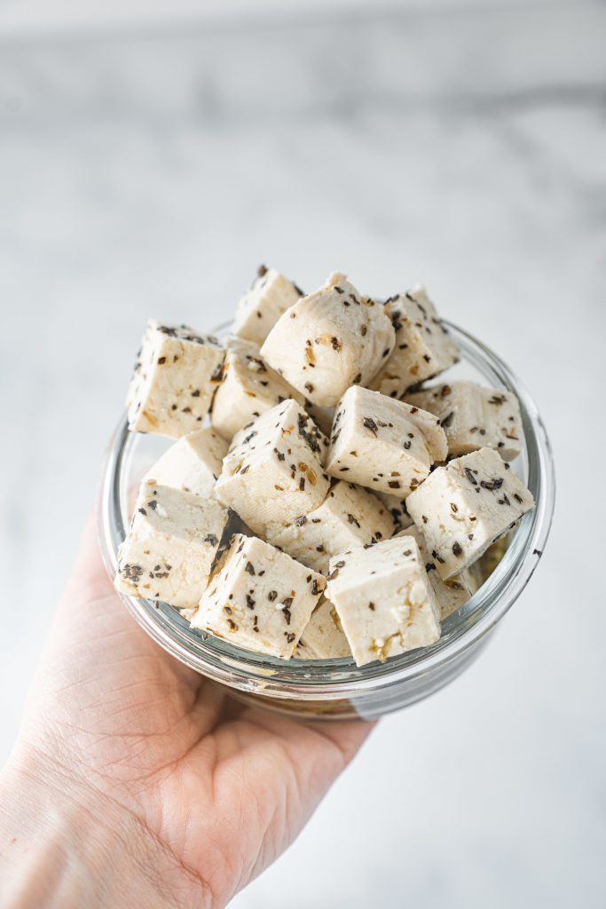 hand holding a bowl of vegan feta cheese with tofu