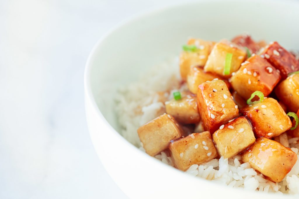 side of a bowl of orange tofu in rice