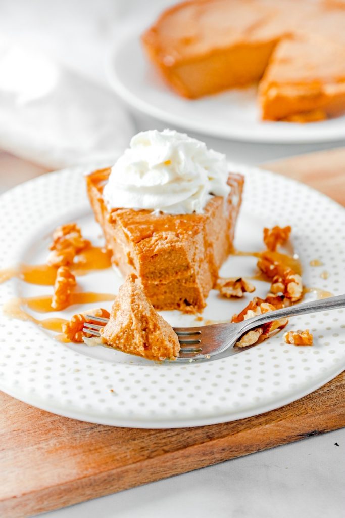 Slice of vegan pumpkin cheesecake on plate topped with whipped cream and caramel with a fork.