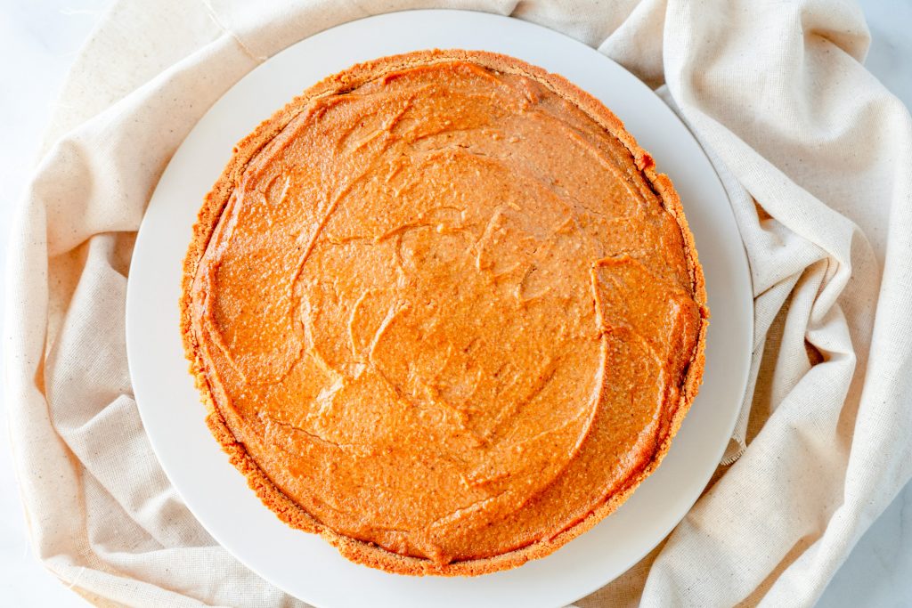 whole tofu pumpkin cheesecake on brown cloth on top of white plate from above