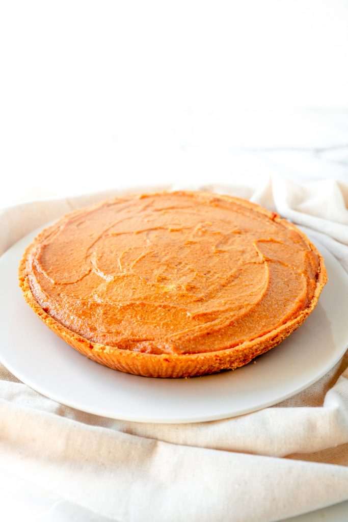 orange eggless pumpkin cheesecake with graham cracker crust sitting on top of a white plate on top of a cloth