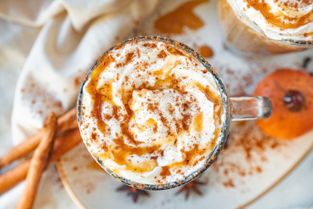 flatlay of vegan pumpkin spice latte with caramel sauce and cinnamon and whipped cream