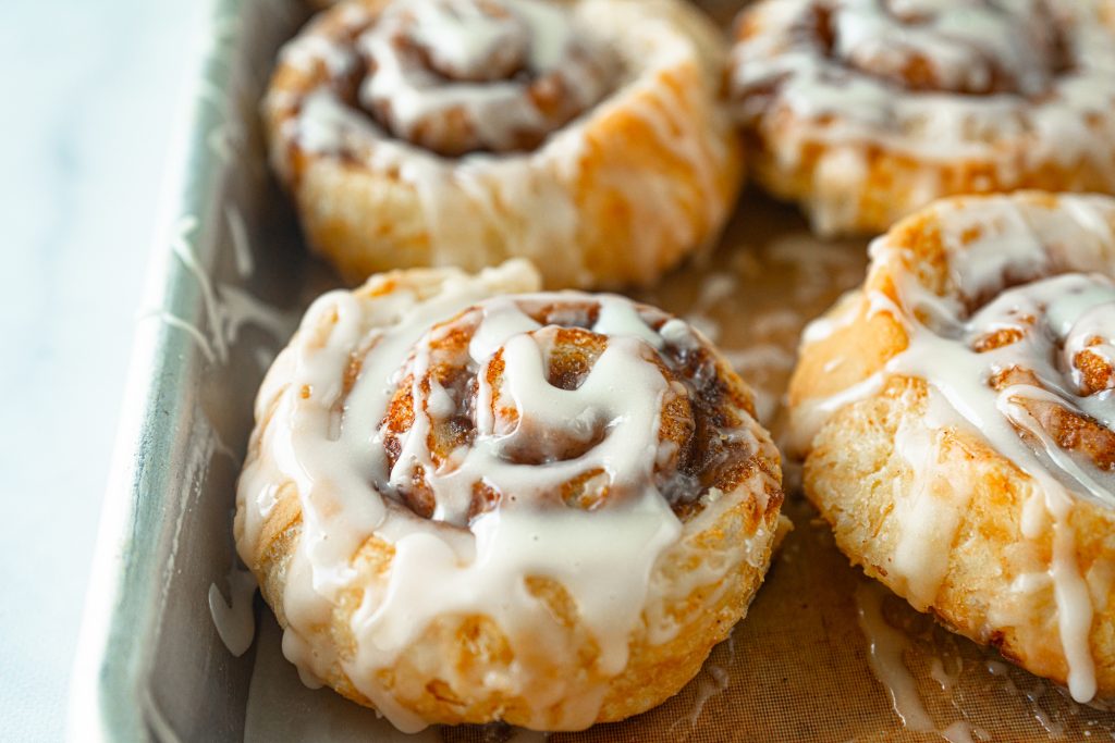 close up of puff pastry cinnamon roll on baking dish with glaze