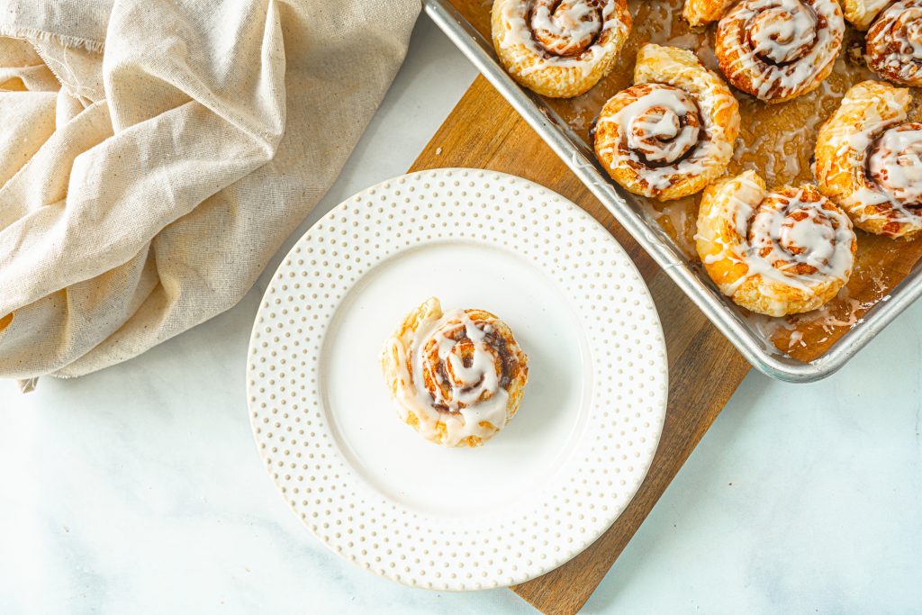 single vegan cinnamon roll on a plate with baking dish next to it