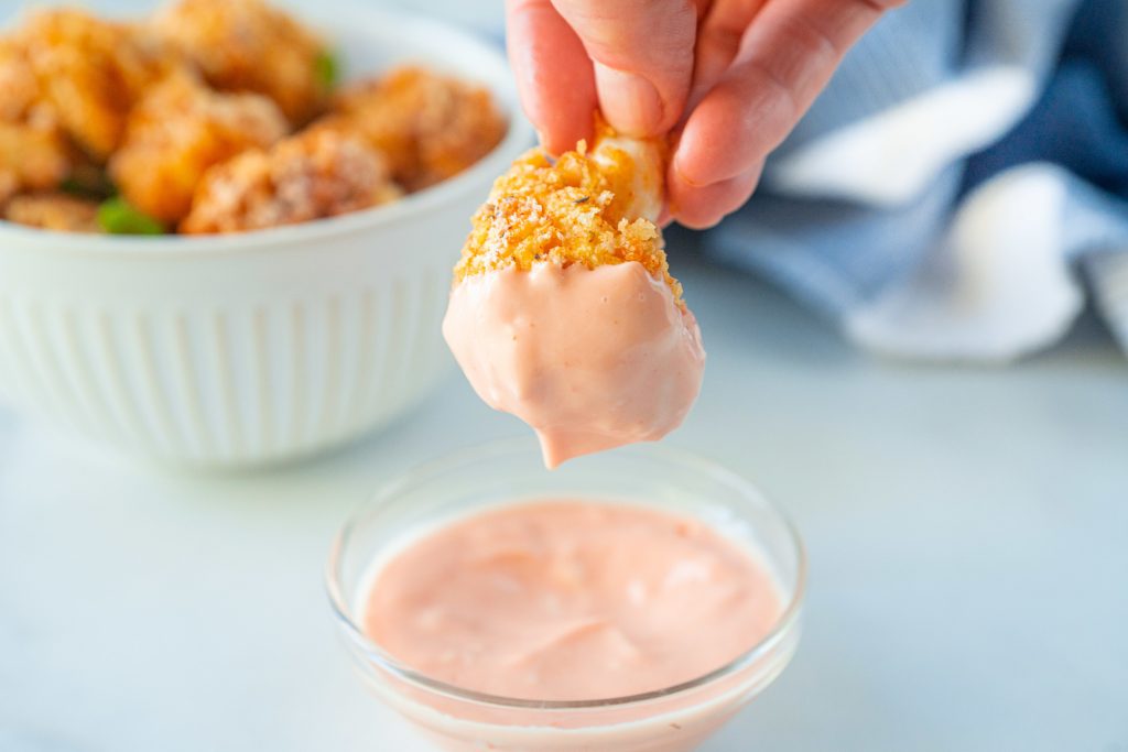 close up of hand dipping piece of crispy cauliflower in sauce