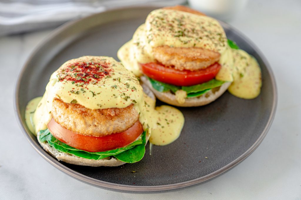 two vegan eggs benedict on a plate with tomato and sauce