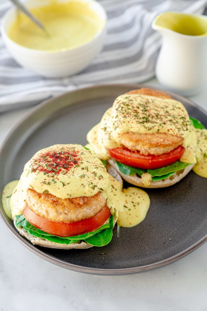 two vegan eggs benedict sandwiches on a plate with sauce in the background