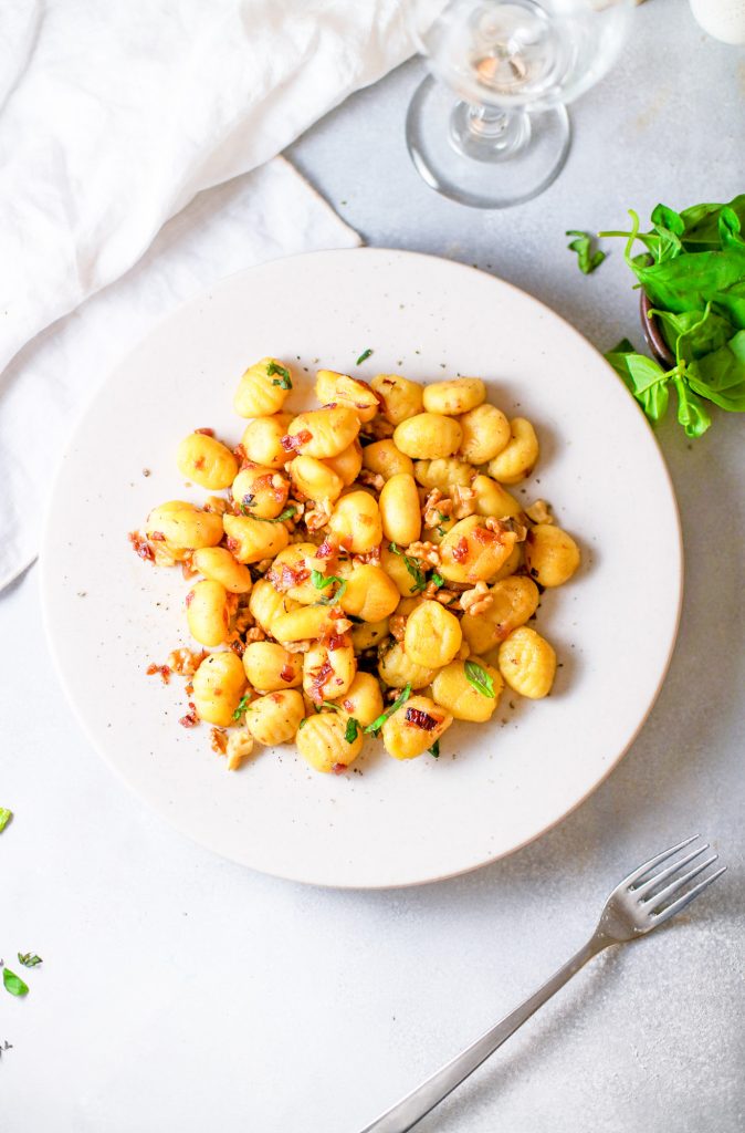 vegan gnocchi recipe on plate with garlic white wine sauce and green basil in the background 