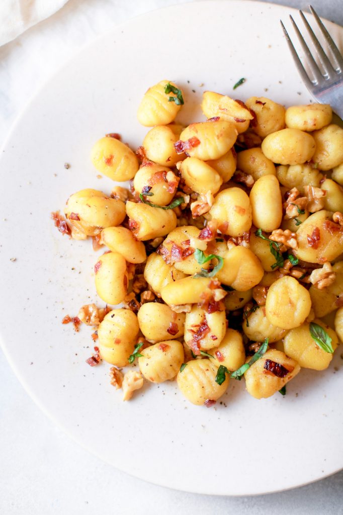 close up of a eggless gnocchi on a white plate with green shavings 