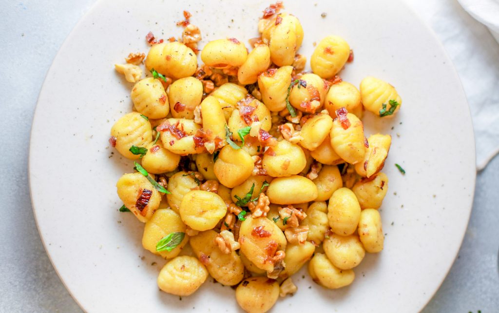 non dairy gnocchi on a plate topped with onions and mushrooms on a white counter with a white cloth