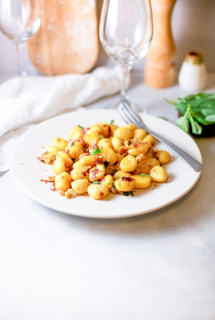 vegan gnocchi on a plate with wine glasses in the background
