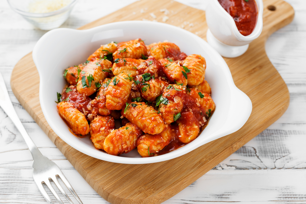 vegan gnocchi tossed in a red sauce in a white bowl with fork 
