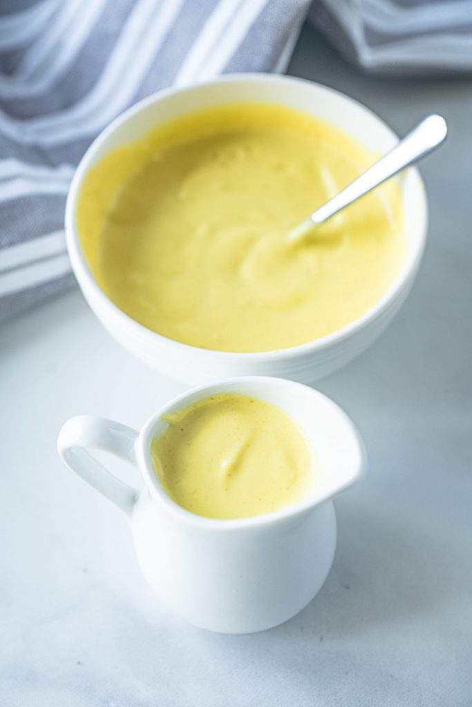 vegan hollandaise sauce in small bowl with spoon and carafe