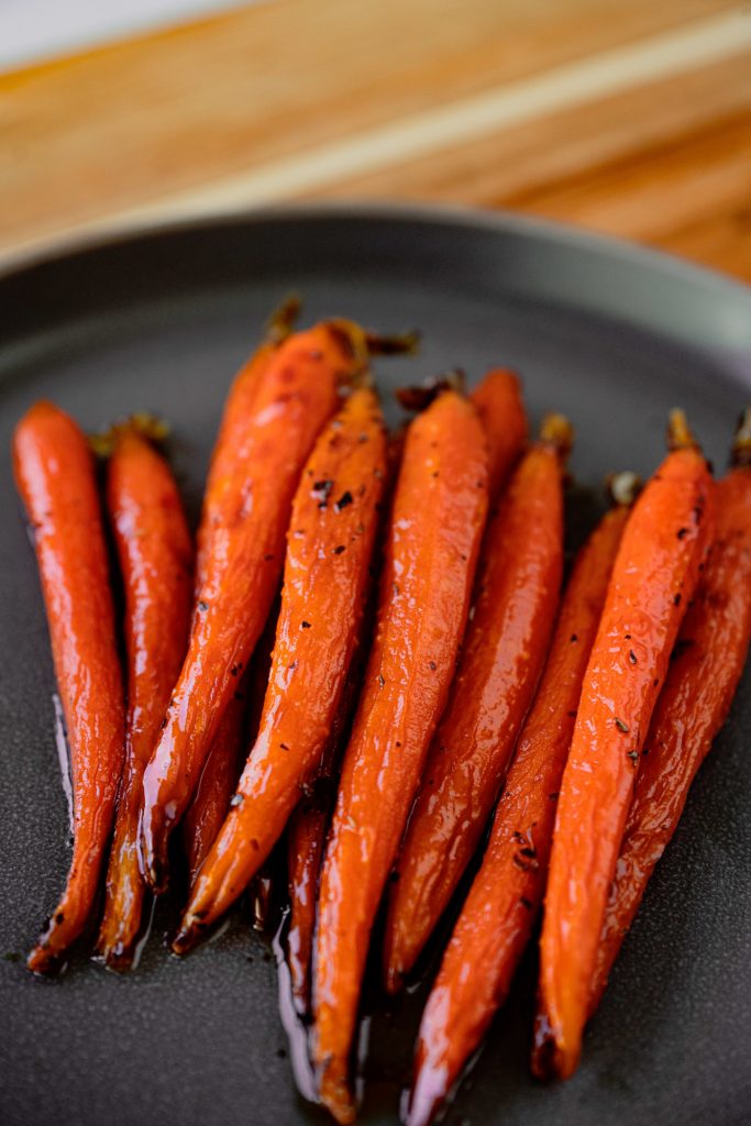 Close up of maple glazed carrots on a black plate.