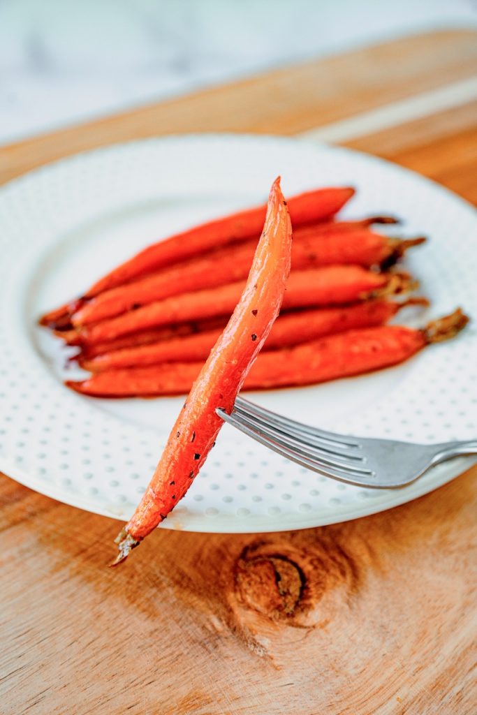 vegan  glazed carrot on the end of a fork with other carrots in the background