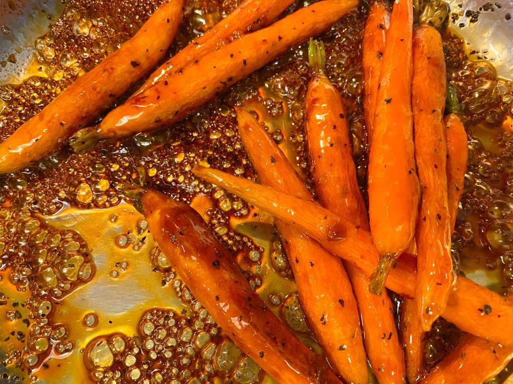 orange carrots being cooked in brown maple sauce in a silver pan 