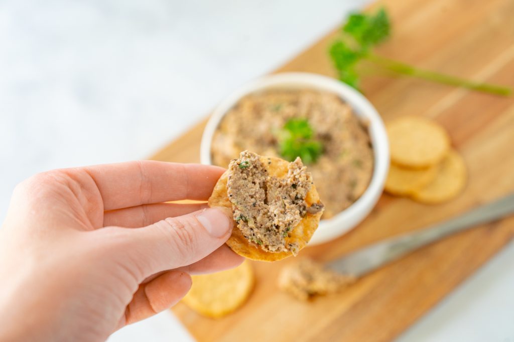 hand holding a cracker with vegan mushroom pate spread on it
