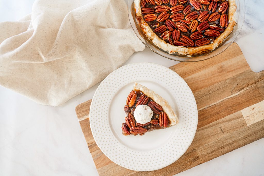 above photo of a slice of vegan pecan pie on a white plate with eggles pecan pie in the background
