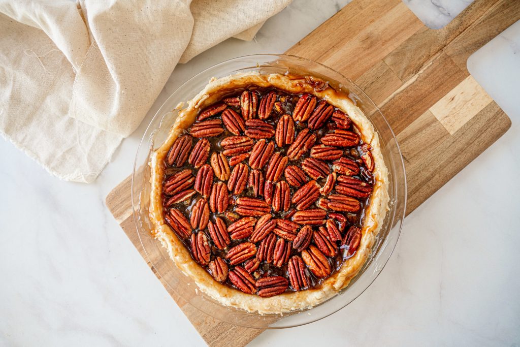 above photo of vegan pecan pie whole and baked on a brown bread board with a white cloth