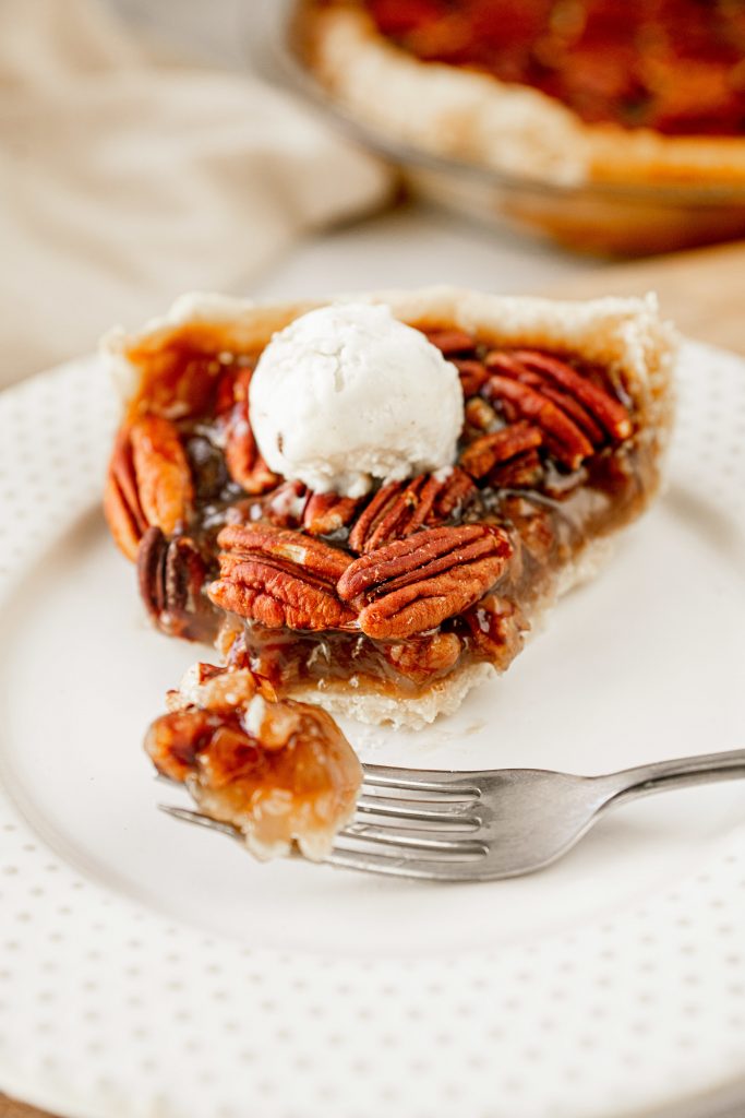 Slice of pecan pie with scoop of vegan ice cream on top with a fork.