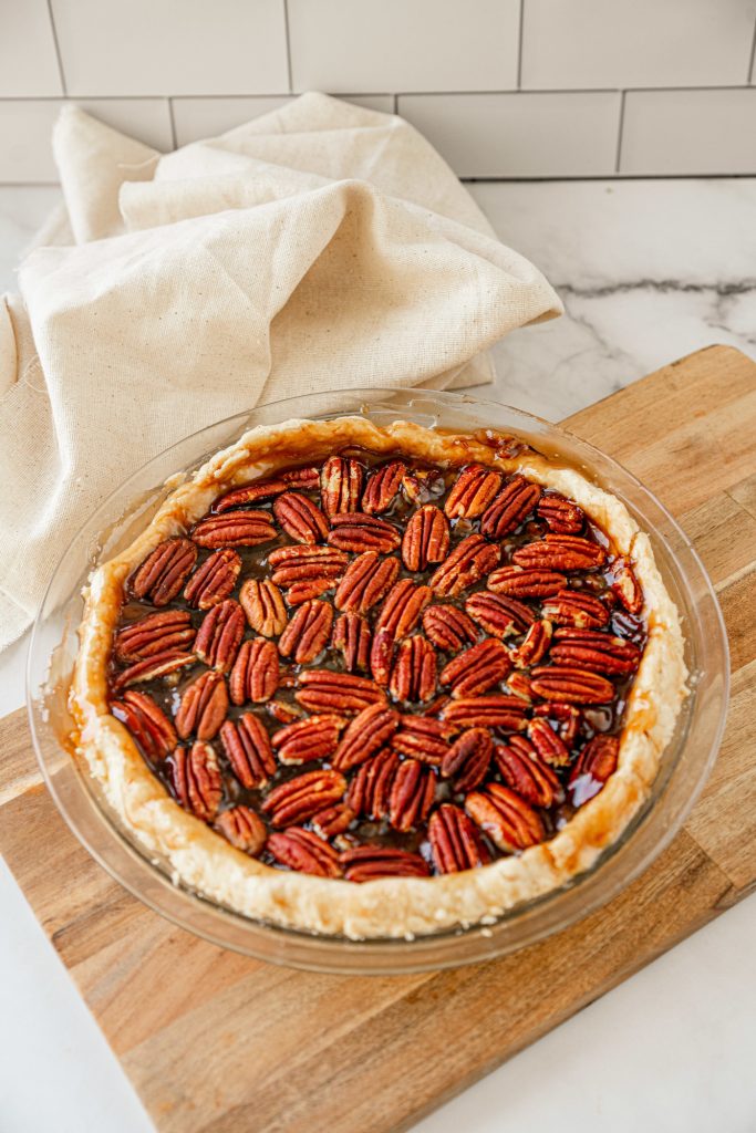 full brown color vegan pecan pie on brown cutting board with dish towel