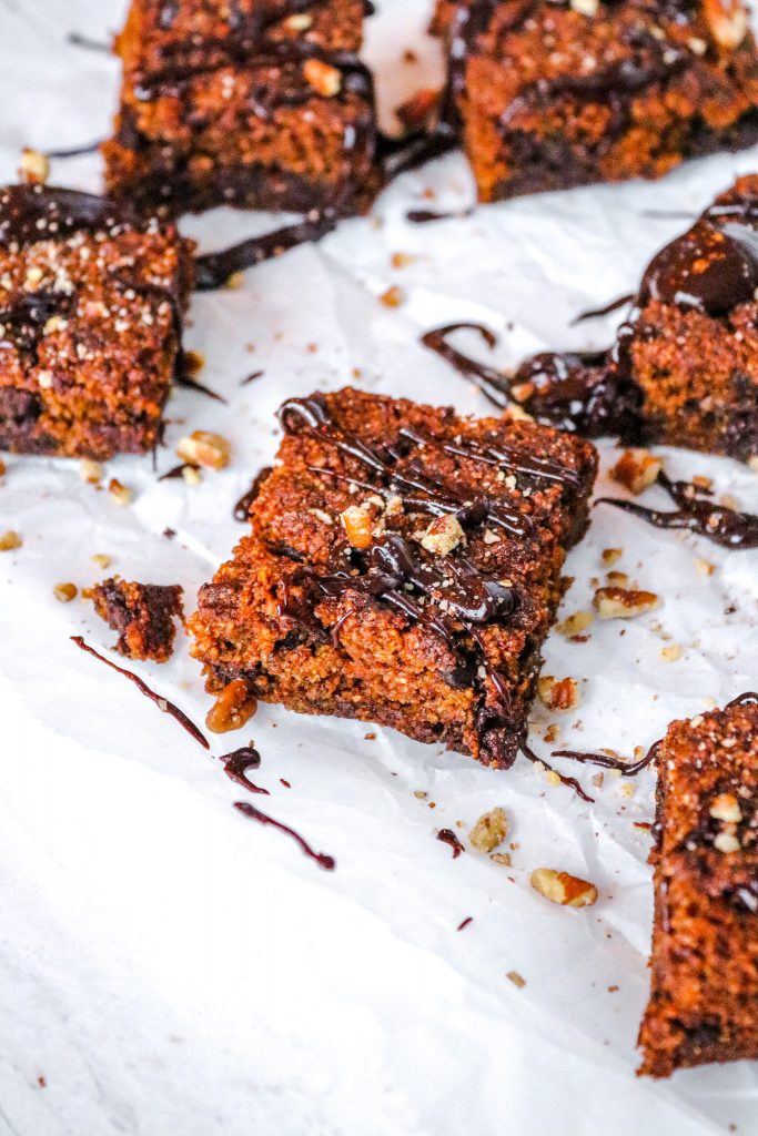 drizzle of chocolate on keto pumpkin brownies with nuts on a white counter with other brownies in the background