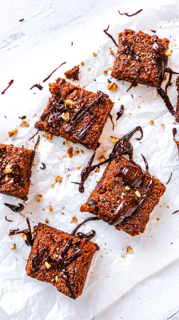 sideways view of vegan pumpkin brownies that are also gluten free and keto on a white surface and topped with light brown nuts