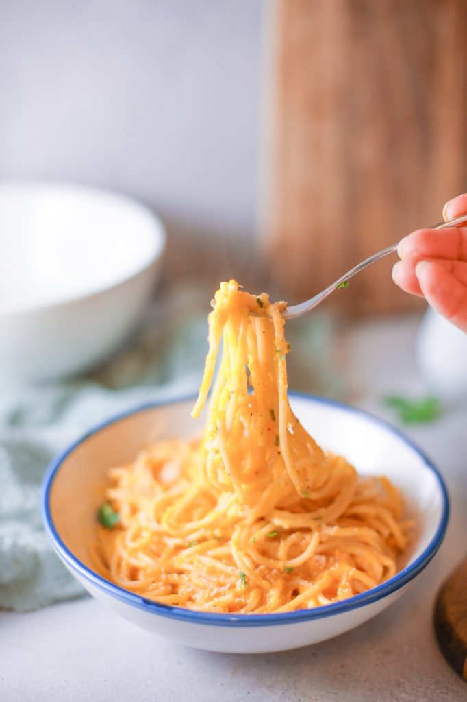 orange pasta with pumpkin sauce twirled around a fork in a white bowl with other bowls in the background