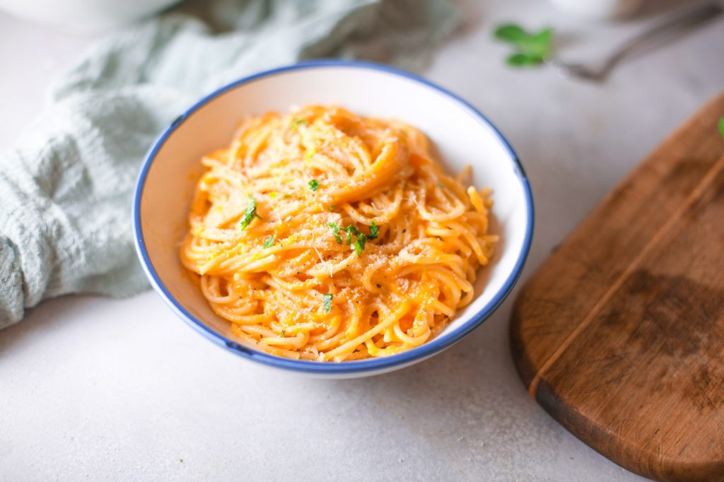 noodles with pumpkin pasta sauce in a bowl with fresh herbs and a cutting board nearby