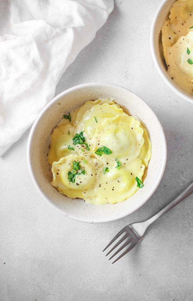 vegan ravioli recipe in a bowl white bowl with parsley and fork laying down on white counter