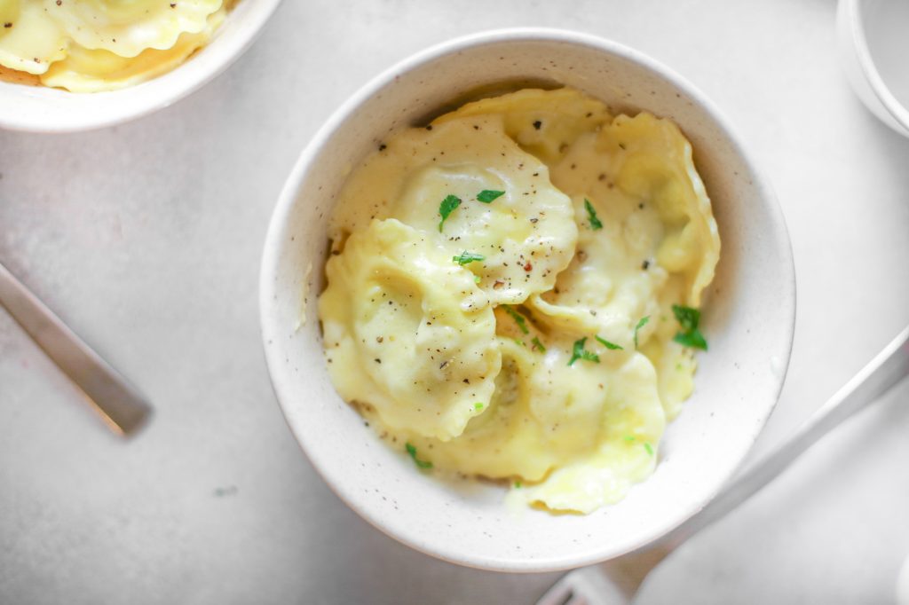 vegan ravioli in a bowl topped with cream sauce and greens