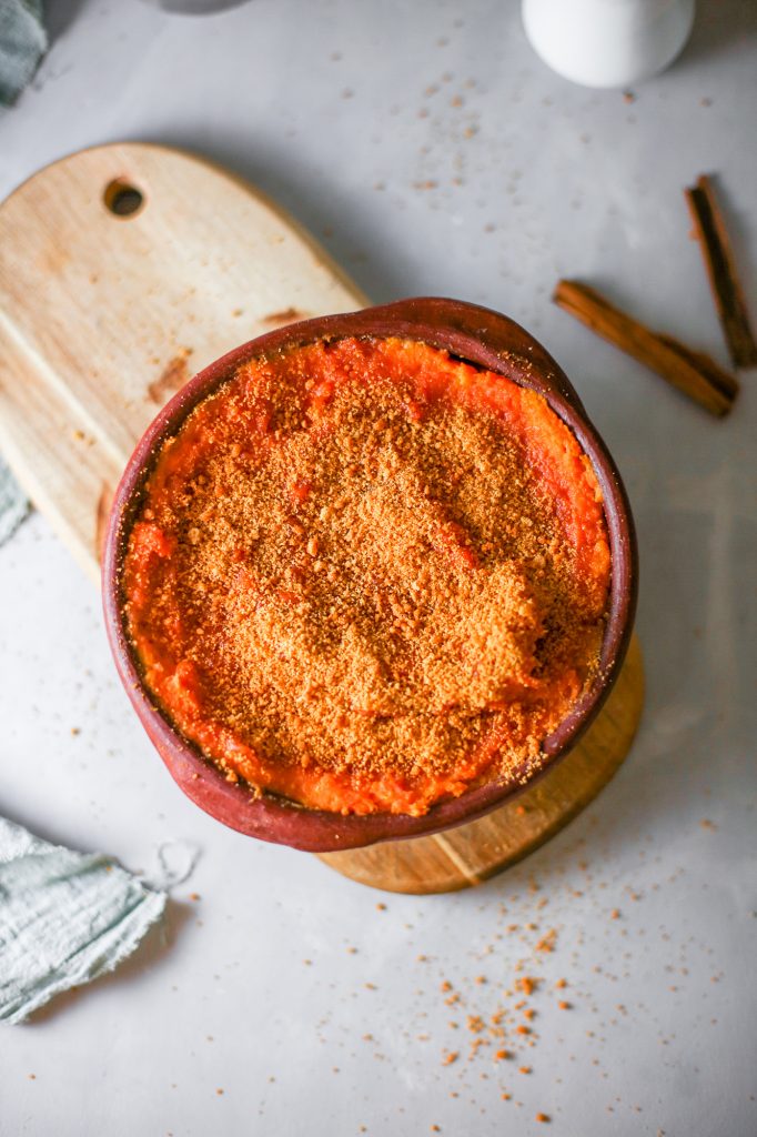 orange colored vegan sweet potato souffle on a brown bread board with crumbs sprinkled on a white counter