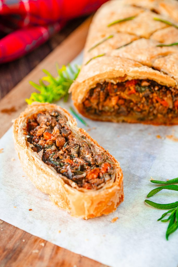 Close up of a slice of vegan wellington with large loaf in the background on a cutting board