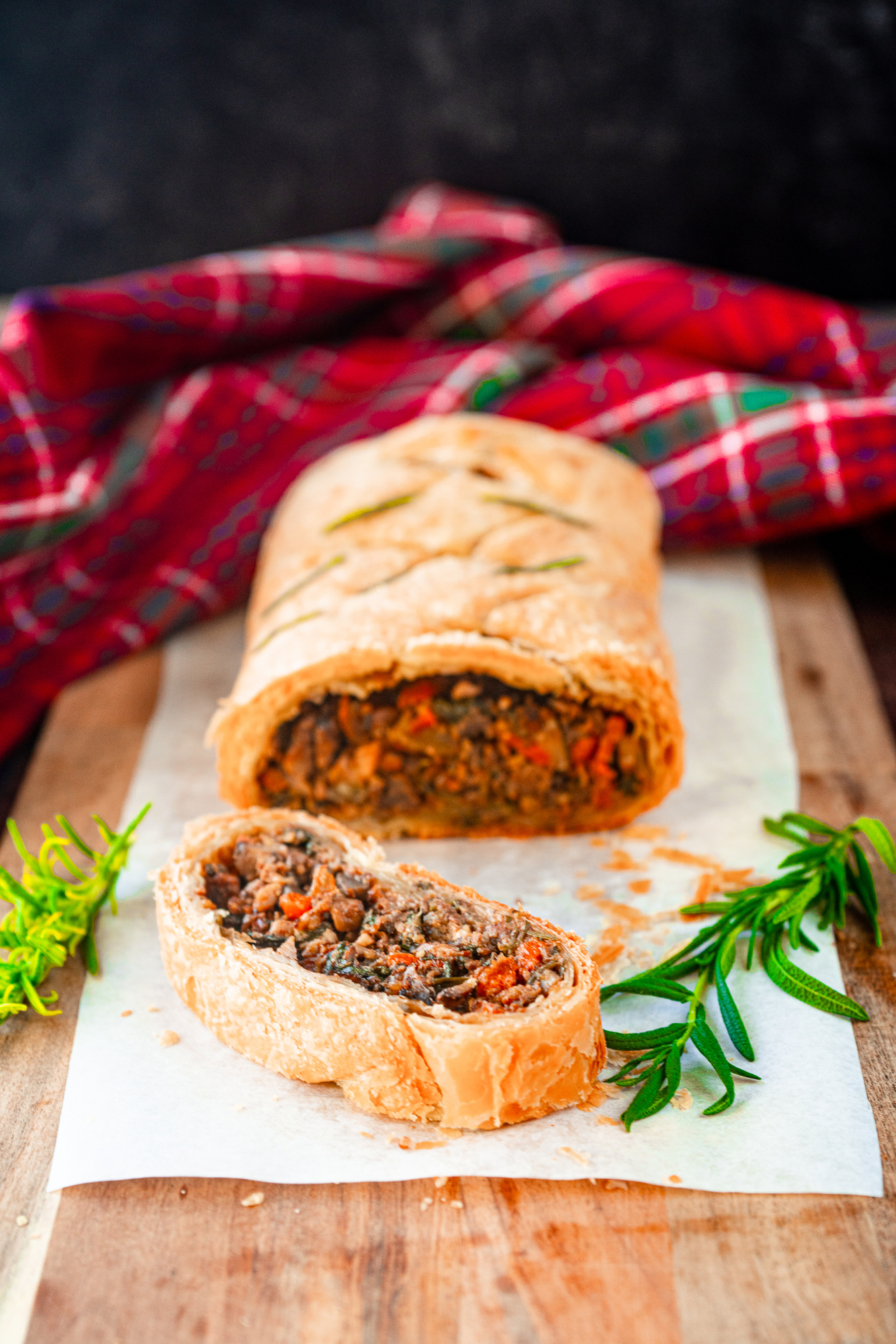 vegan wellington with mushrooms cut into slices with rosemary with a tartan cloth in the background.