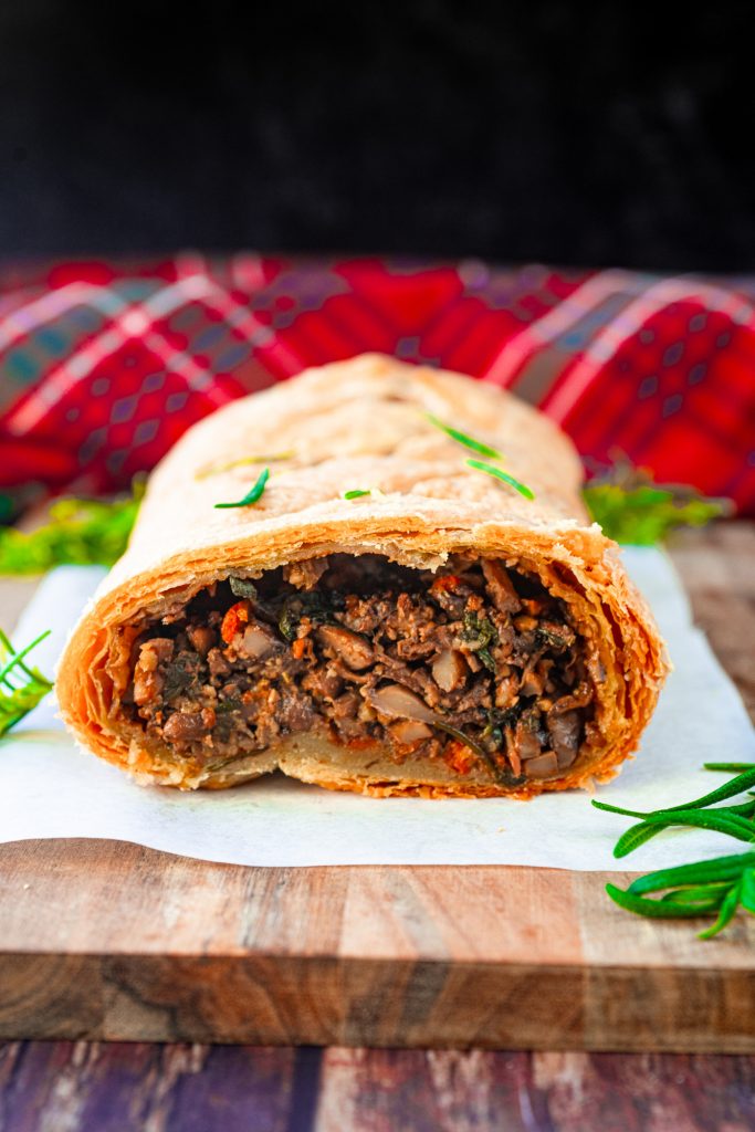 Close up of the inside of a vegan wellington with mushrooms sliced with red dish cloth in the background.