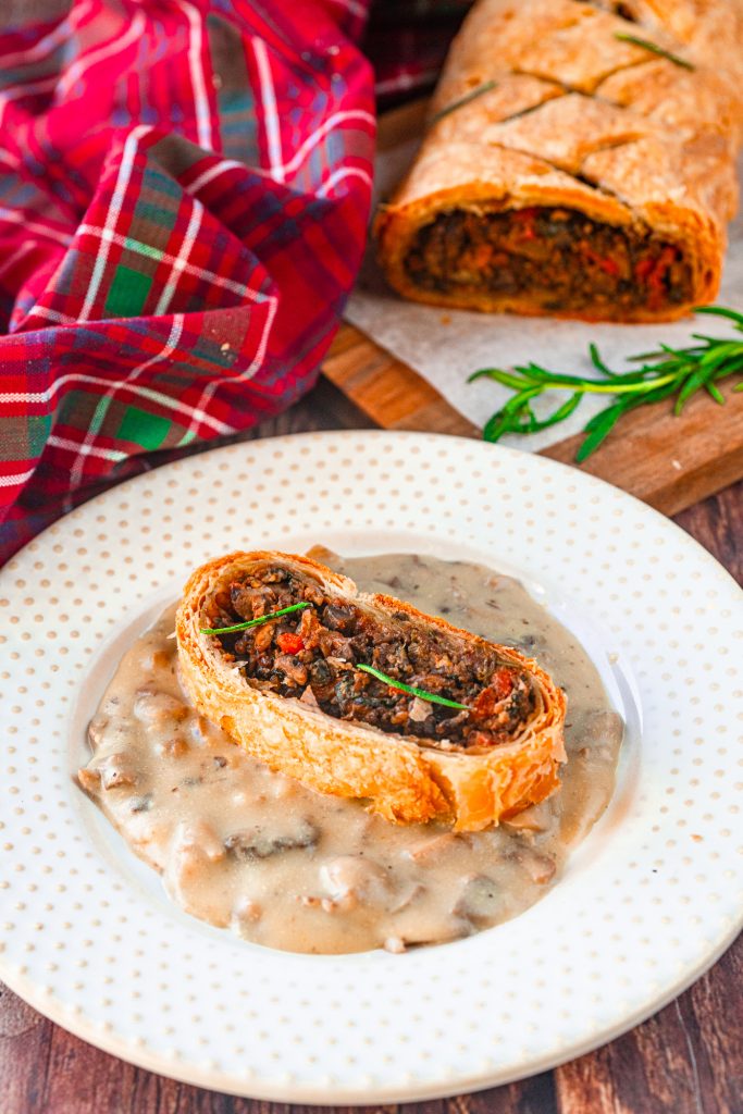 slice of vegan mushroom wellington on mushroom brown gravy on a white plate