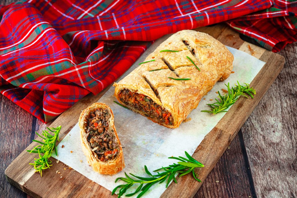 vegan wellington with a slice cut out of it on a cutting board next to a tartan cloth.