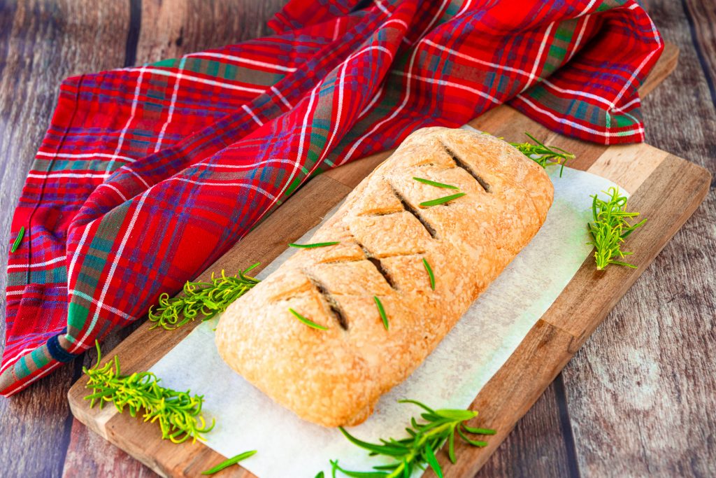 whole vegan wellington with christmas towel on a piece of parchment paper on top of a brown cutting board