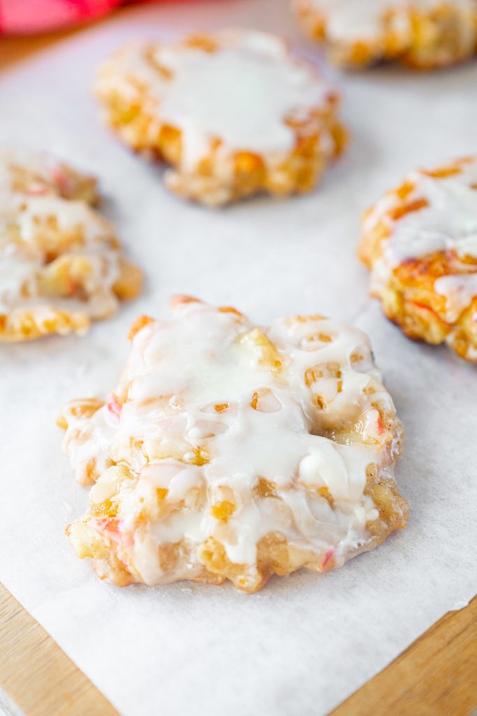 vegan apple fritters covered in white glaze cooling on parchment paper