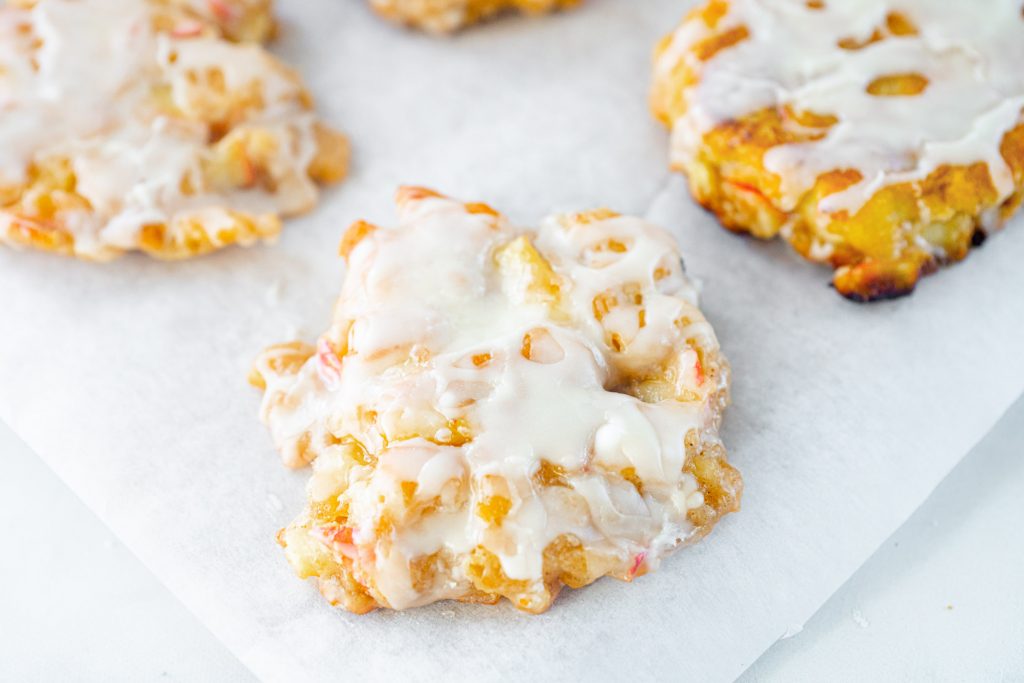 A close up of glaze on vegan apple fritters on parchment paper.